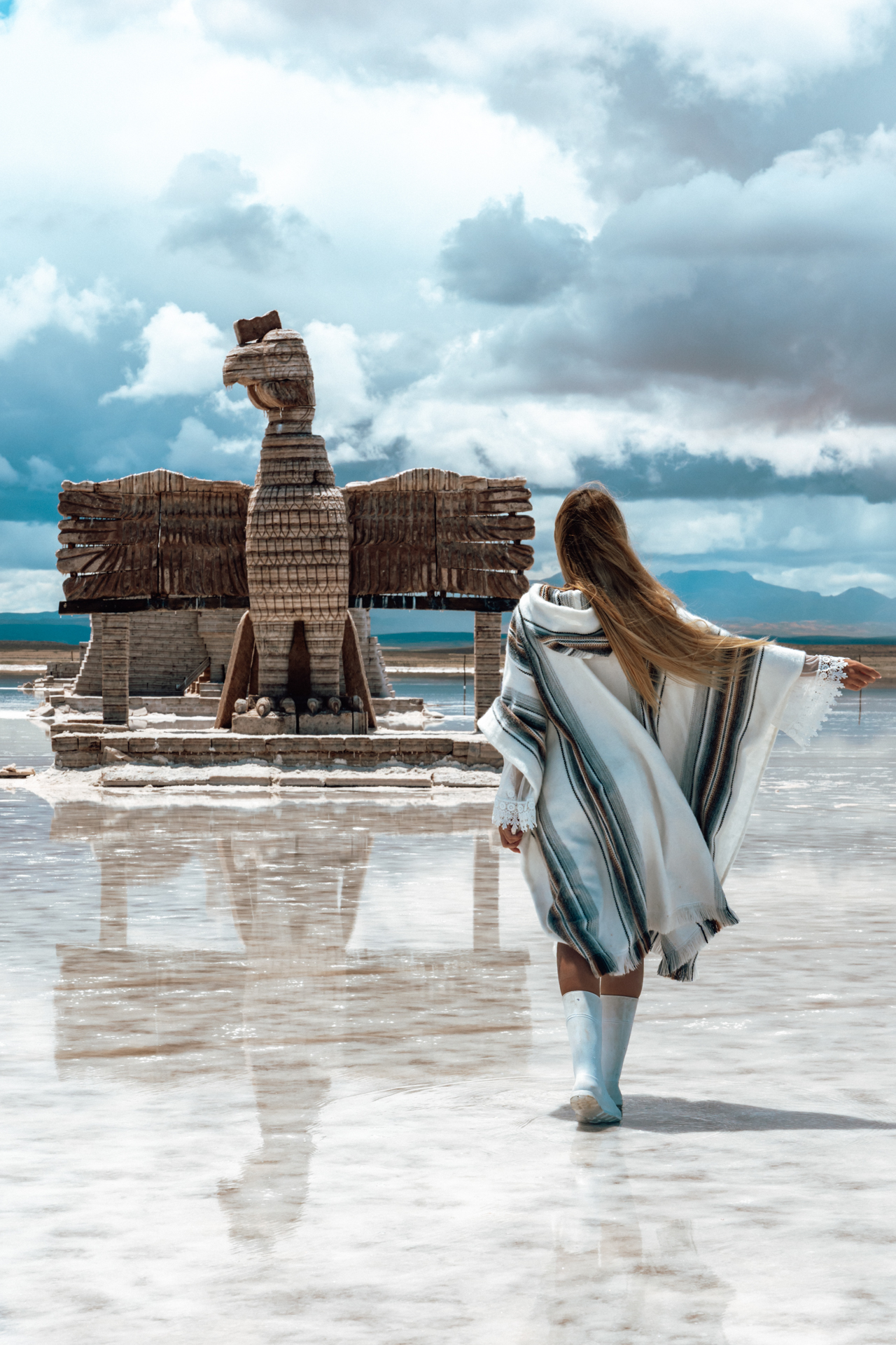 Uyuni Salt Flats Woman in poncho walking to giant eagle sculpture on Uyuni Salt Flats, Bolivia
