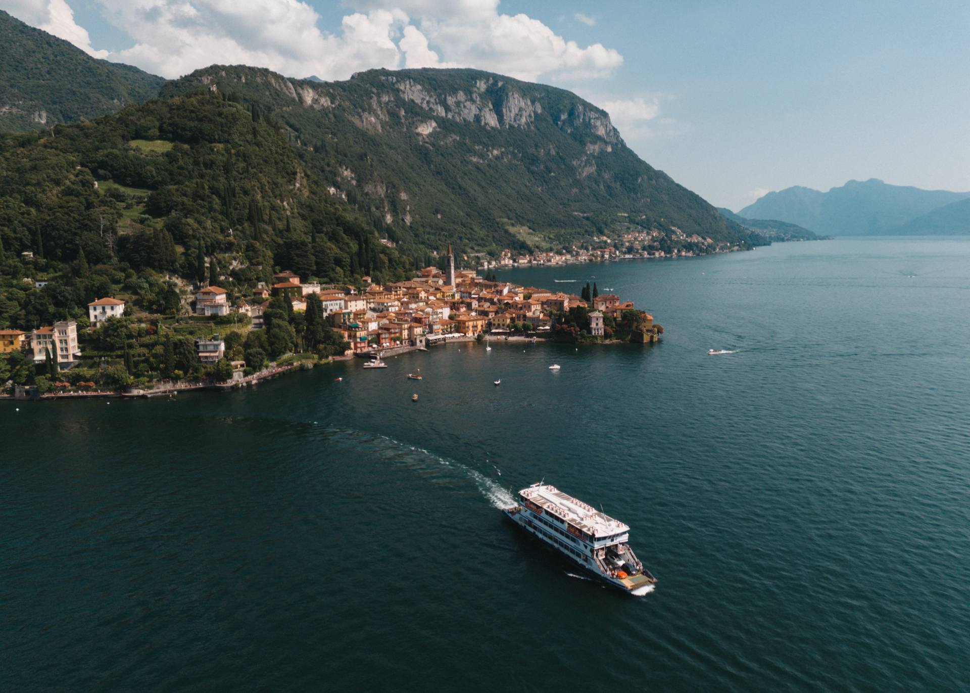 Varenna Aerial drone view of Varenna town and Lake Como shoreline with colorful houses, marina, and surrounding mountains.
