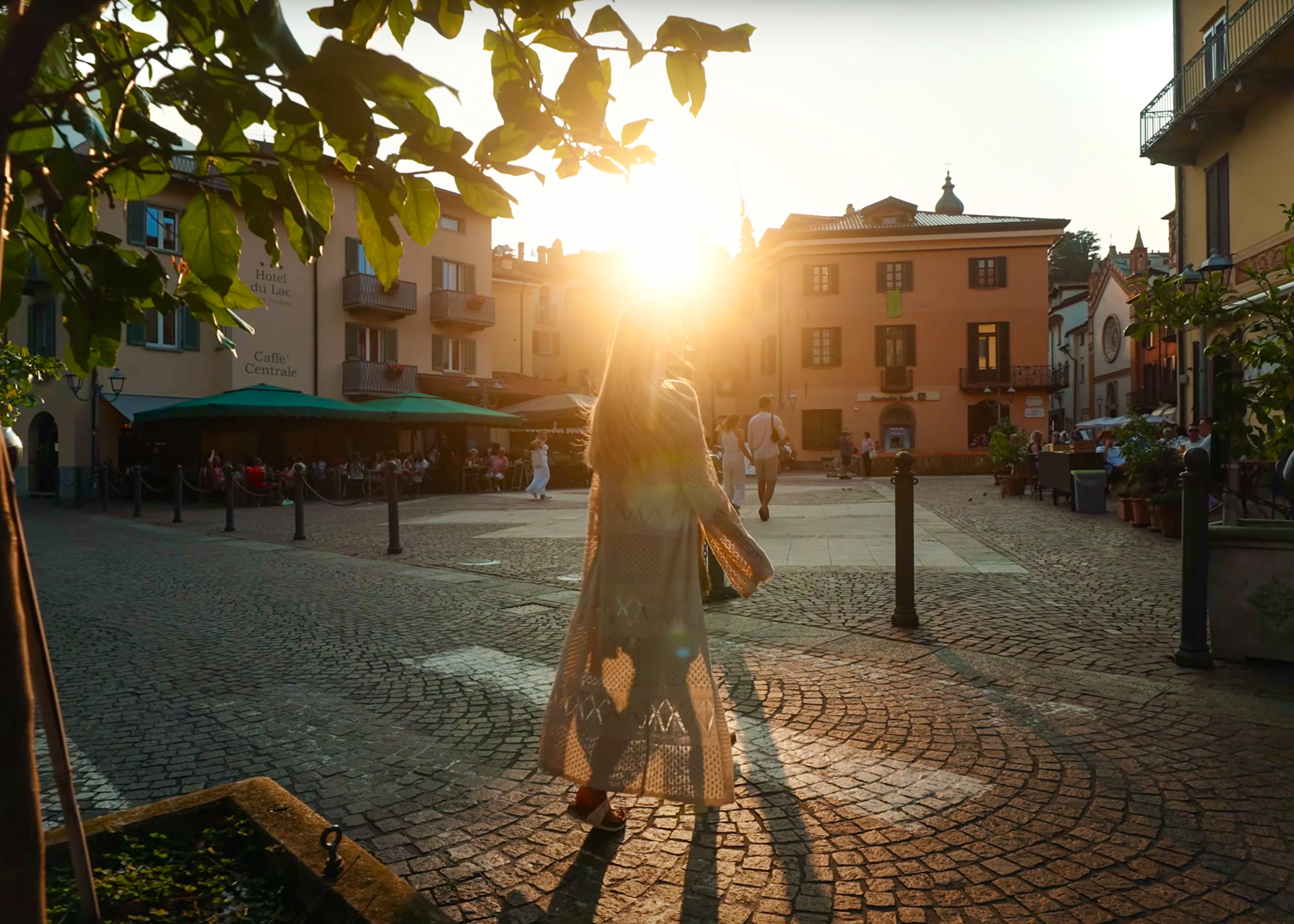 Woman walking into Menaggio’s historic square at sunset with golden sunlight shining through, Lake Como, Italy.