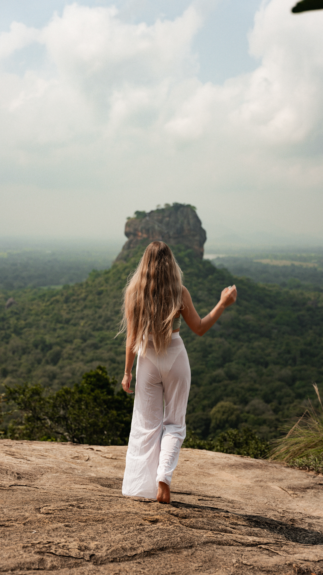 Sigiriya Woman in white walking barefoot on a Pidurangala rock with Lion's Rock rising from the jungle in Sri Lanka