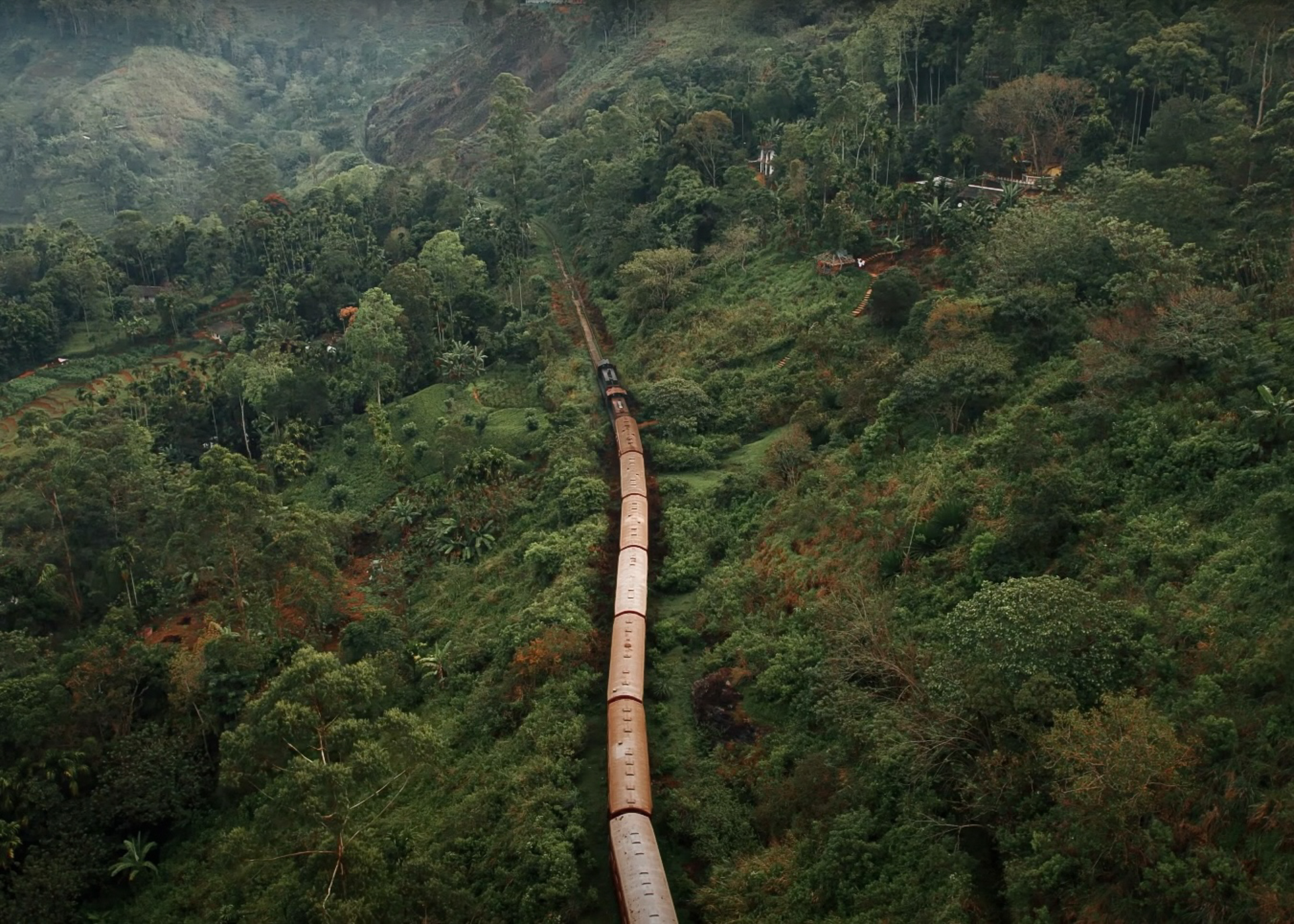 Scenic aerial view of a train passing through lush green hills and tea plantations in Sri Lanka.