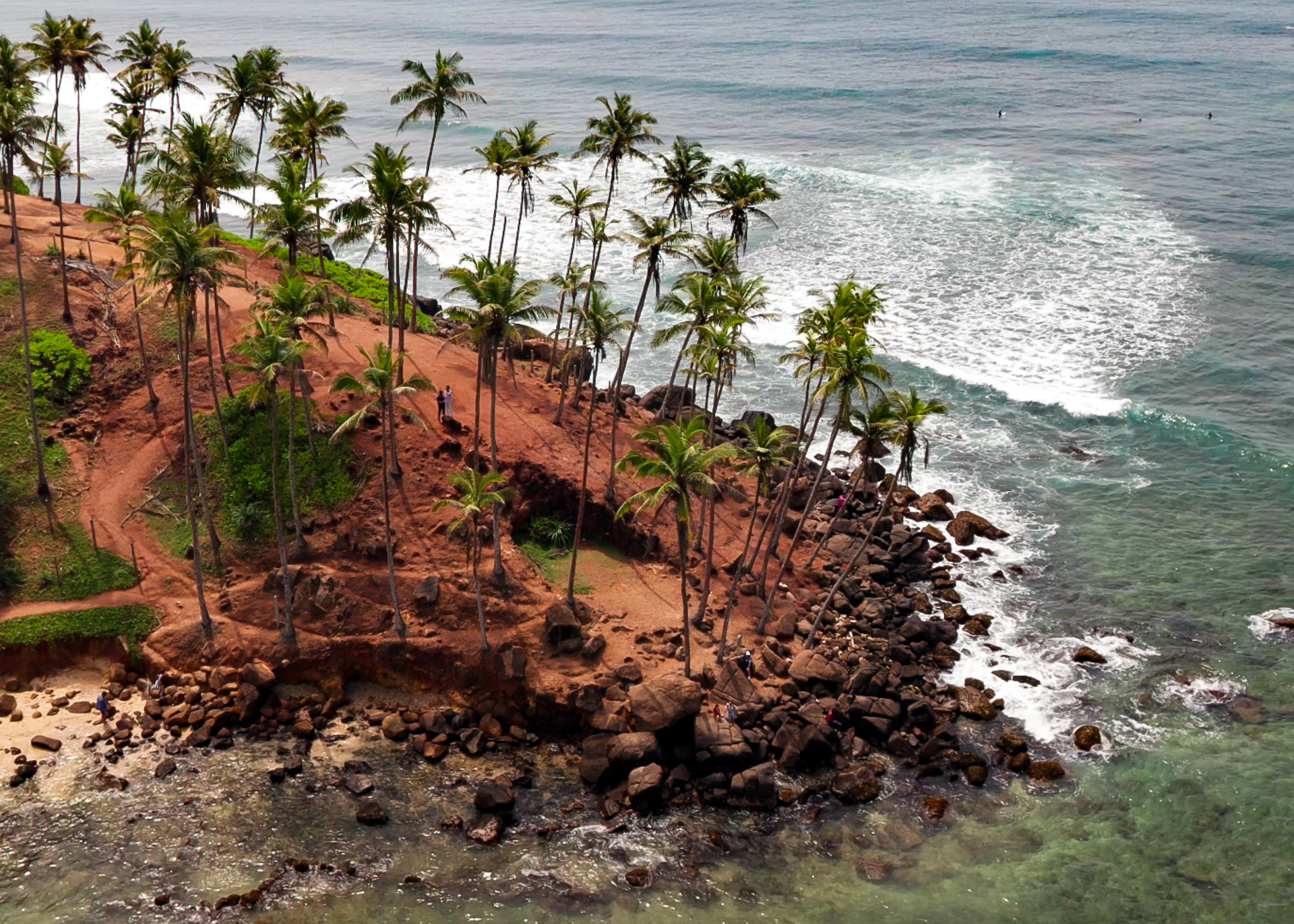Aerial view of Coconut Tree Hill in Mirissa, Sri Lanka, with tall palm trees on a red cliff overlooking the ocean.