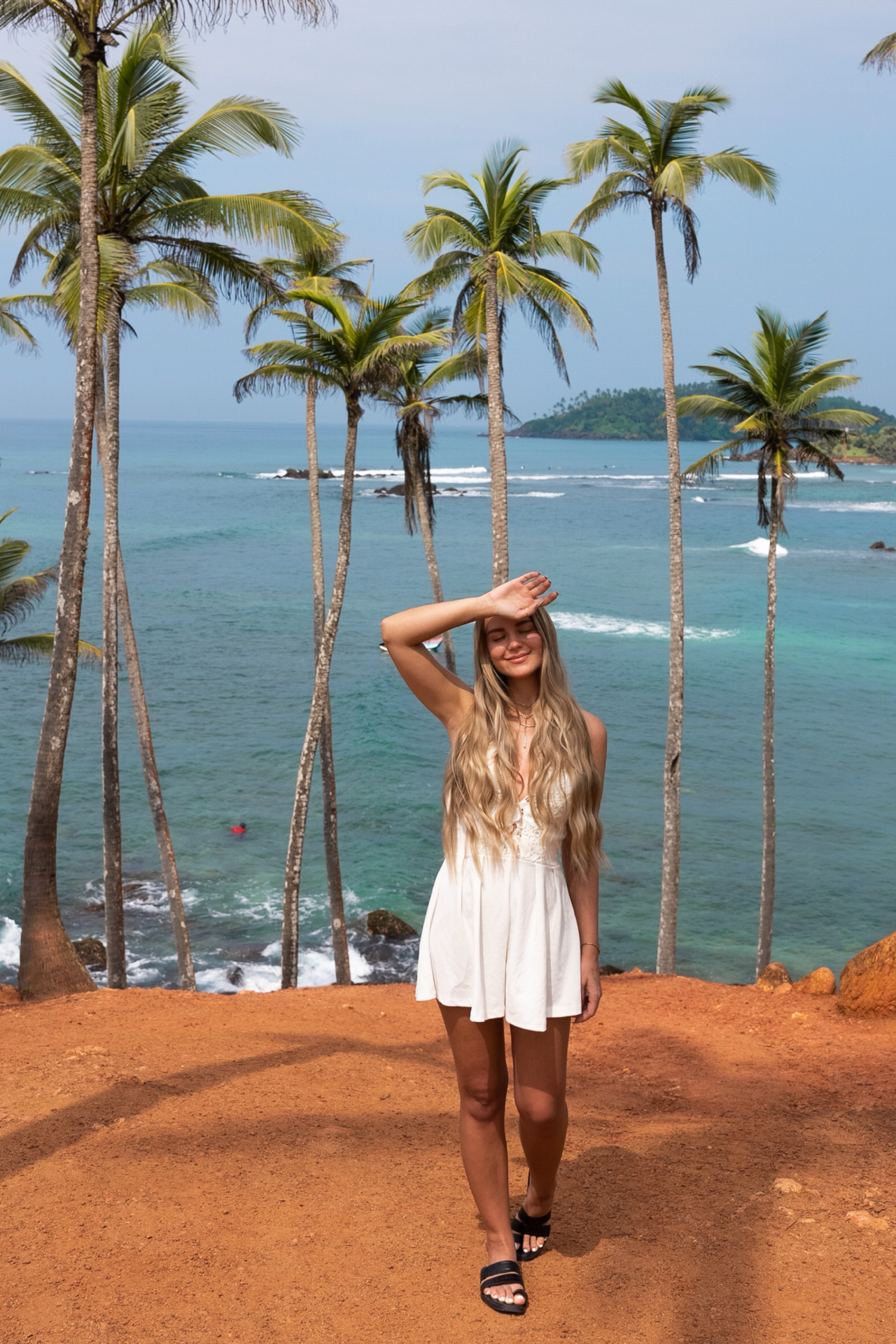 Woman standing under palm trees at Coconut Tree Hill in Mirissa, overlooking the turquoise Indian Ocean.
