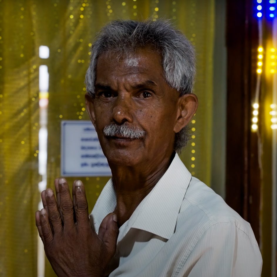 Traditions in Sri Lanka Portrait of an elderly Sri Lankan man greeting with hands together inside a colorful temple in Kandy