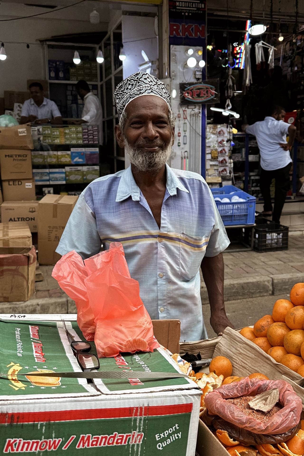Smiling street vendor selling fresh oranges at a market stall at Pettah Market in Colombo, Sri Lanka.