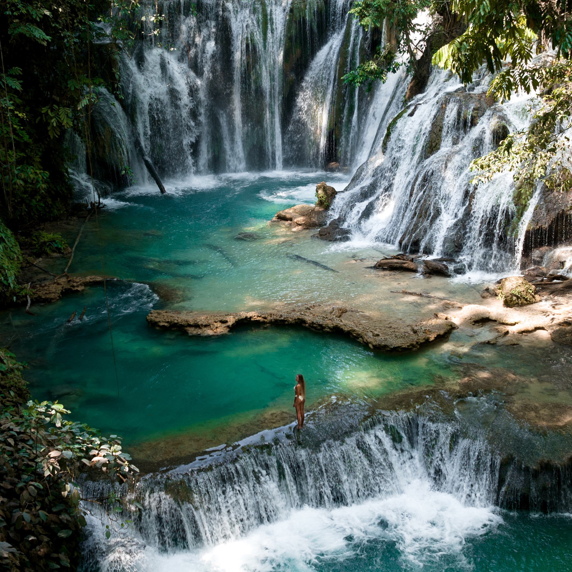 Woman standing by turquoise natural pool at Piala waterfall in Luwuk Sulawesi, Indonesia