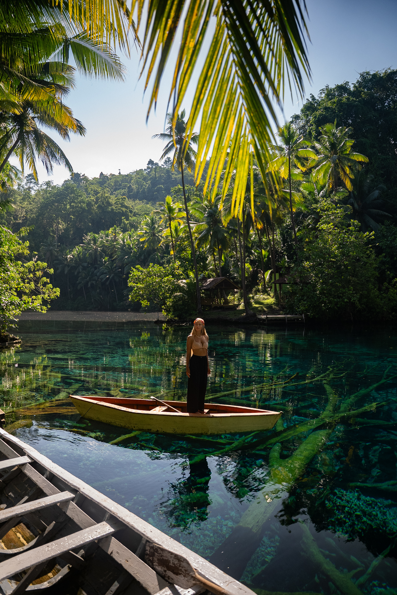 Woman standing on a wooden boat floating on a clear turquoise lagoon in Banggai, Indonesia.