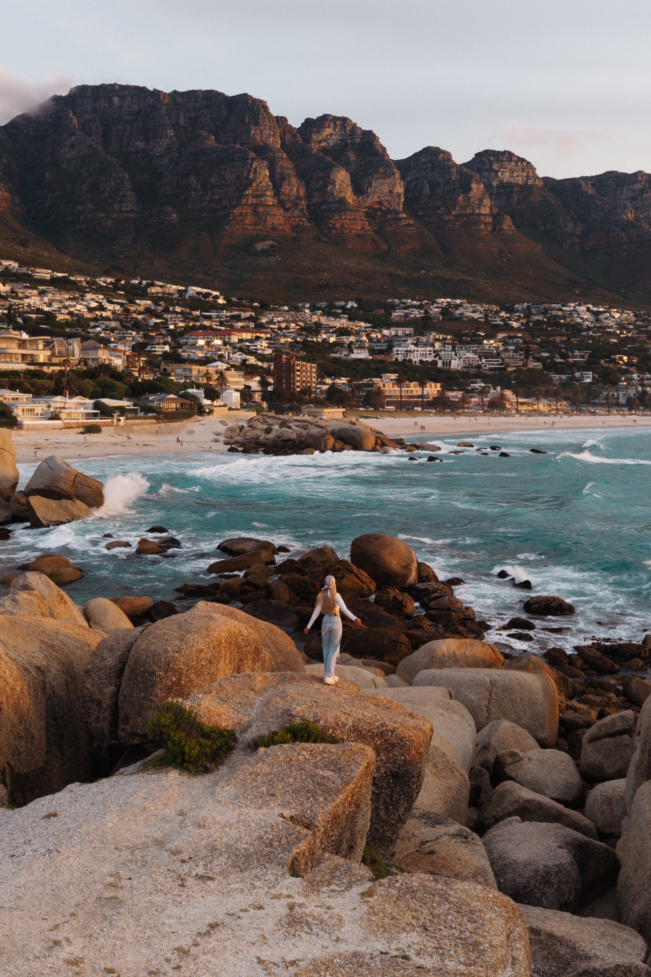 Camps Bay Woman standing on rocks with ocean and Twelve Apostles in view at camps Bay.