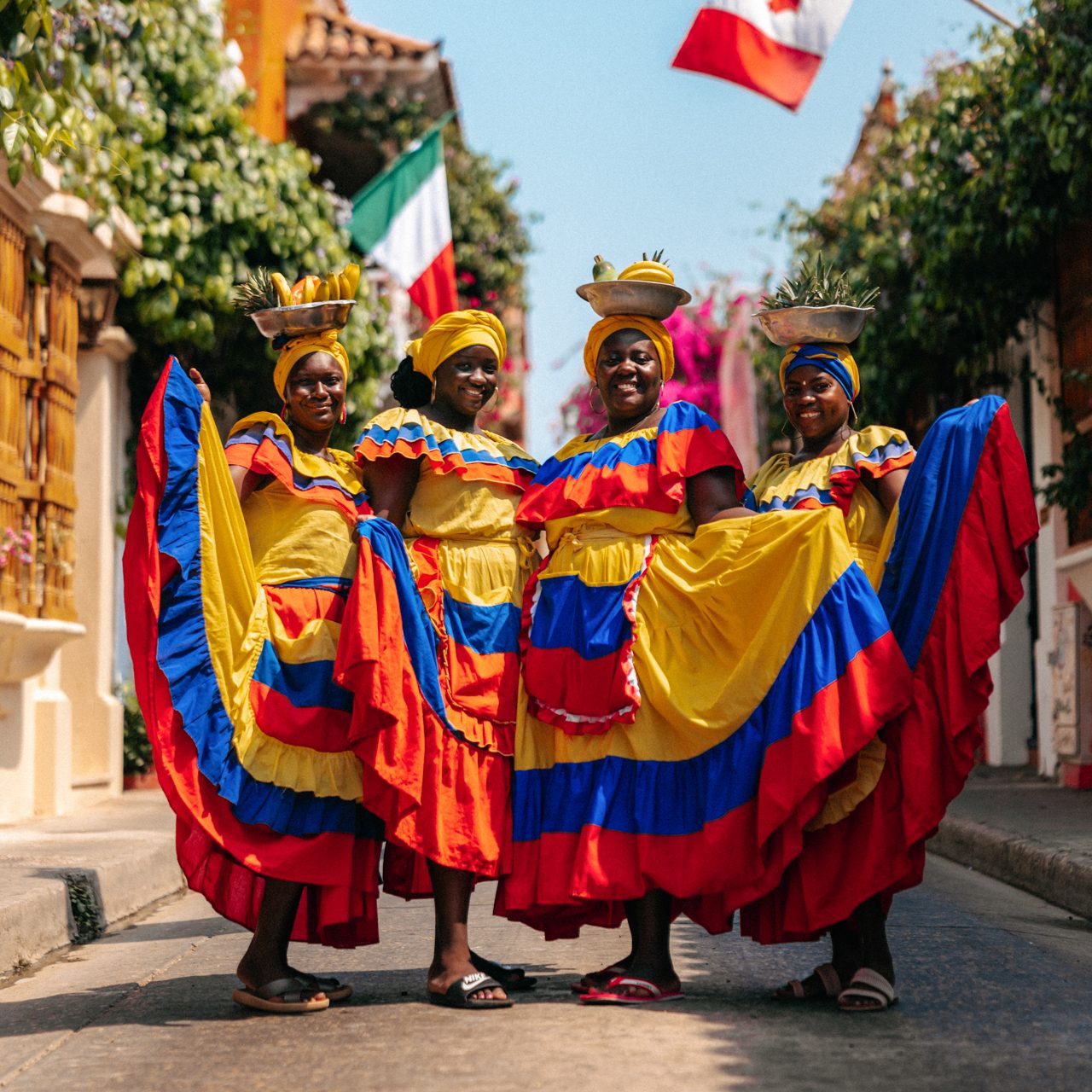 Culture in Colombia Group of Afro-Colombian women in traditional colorful dresses posing with fruit baskets on their heads in Cartagena, Colombia.