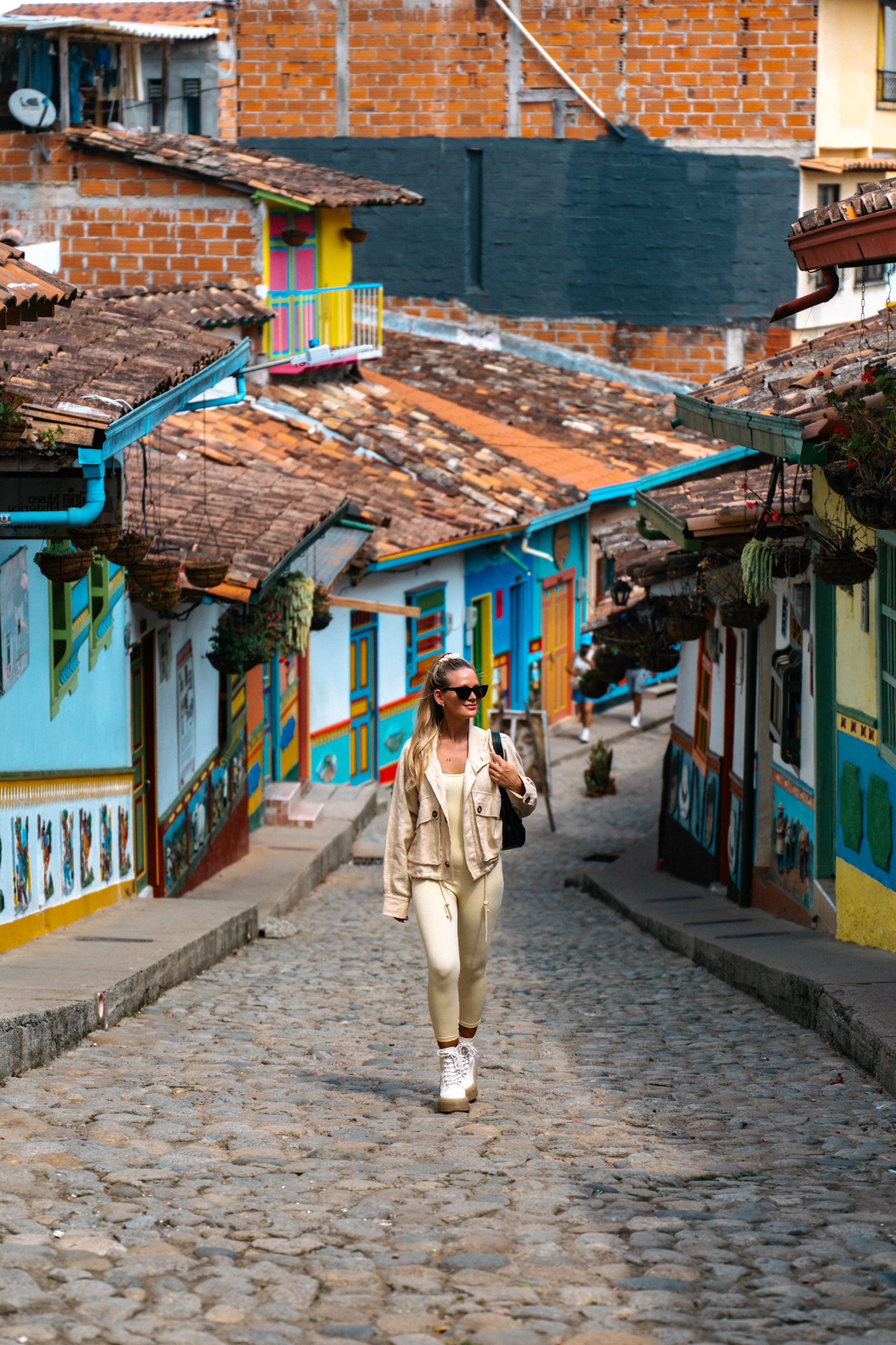Guatape Traveler walking along a cobblestone street lined with colorful houses in Guatapé, Colombia