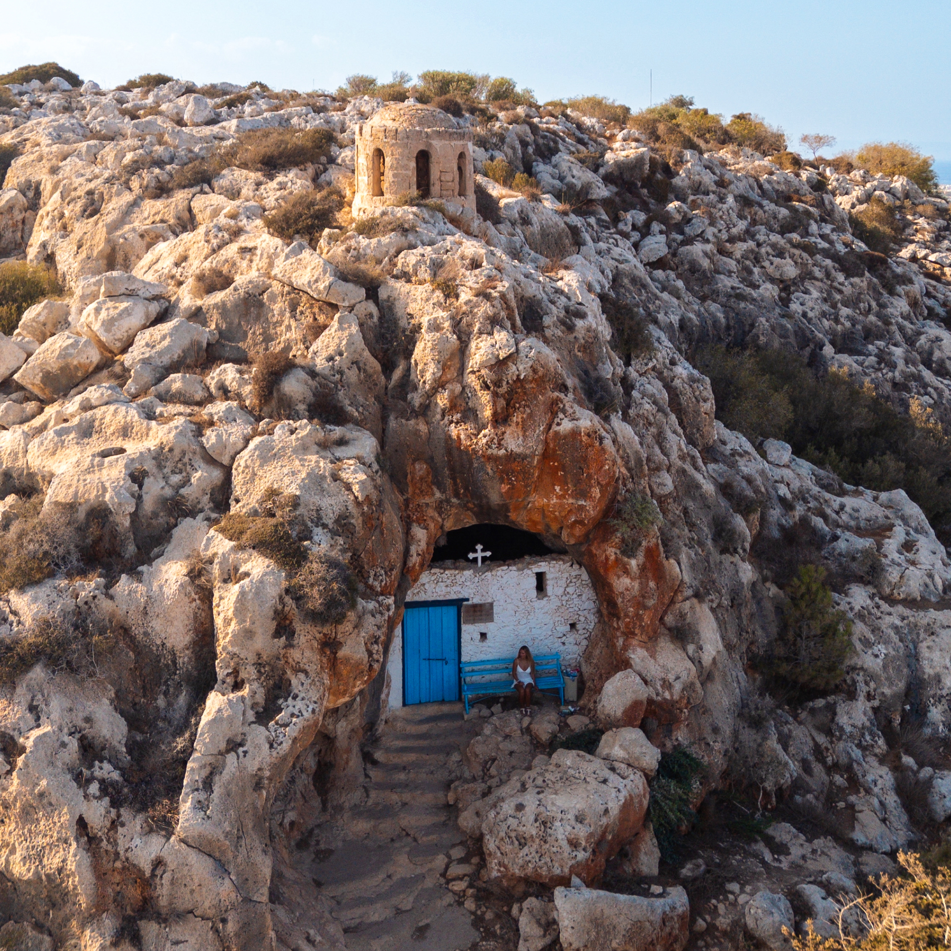Small stone chapel built into rocky hillside with blue door in Cyprus.