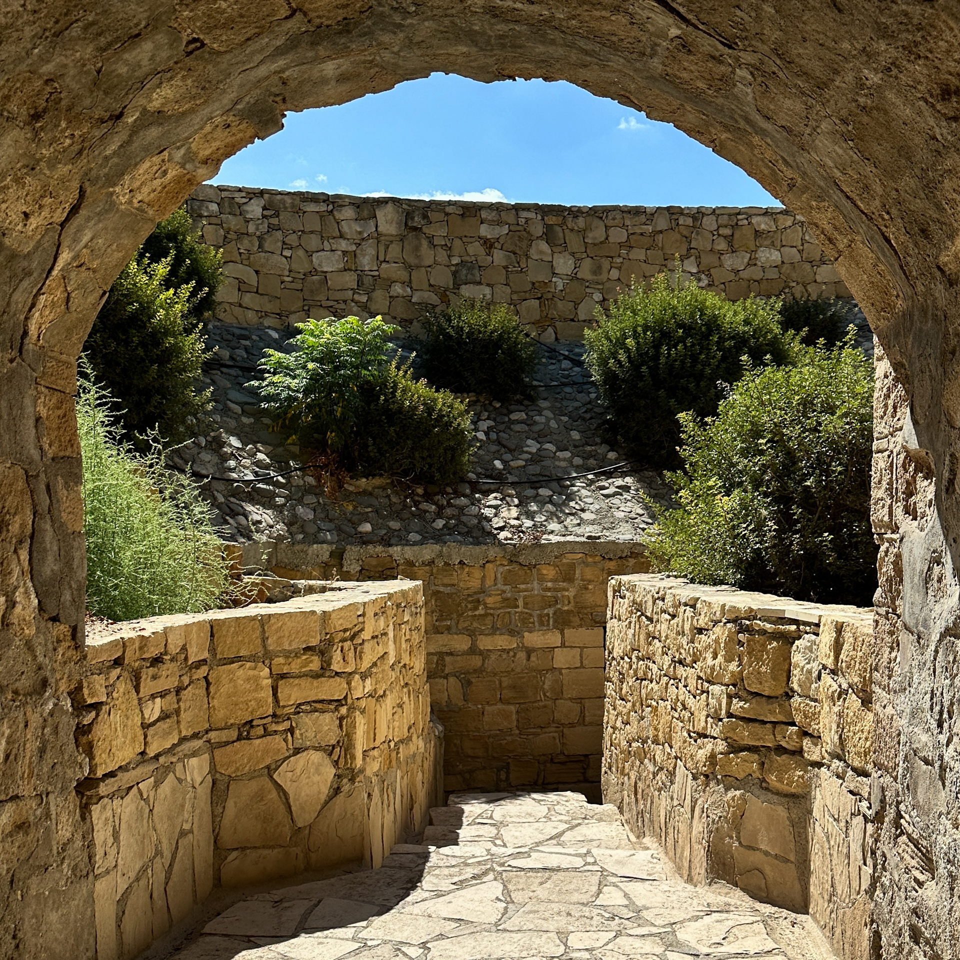 Stone archway and pathway at Kolossi Castle in Cyprus, with sunlit walls and greenery in the background.