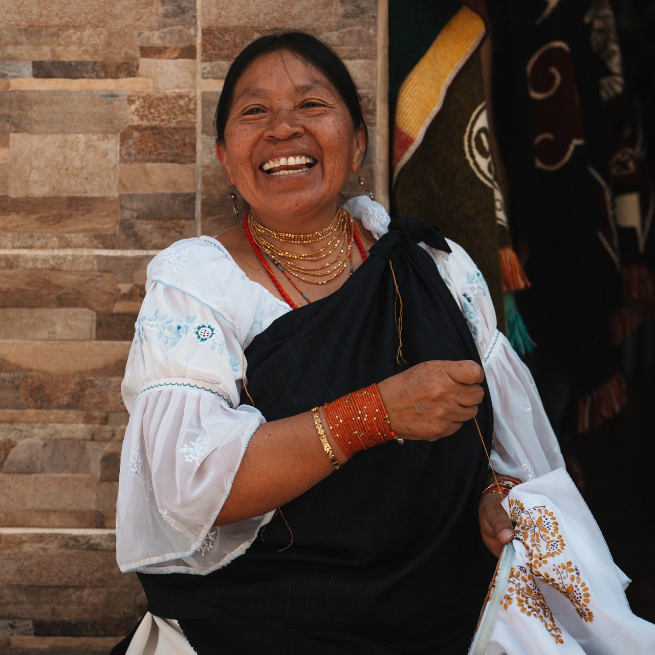Culture in Ecuador Indigenous woman in traditional clothing smiling while doing embroidery at a market in Ecuador.
