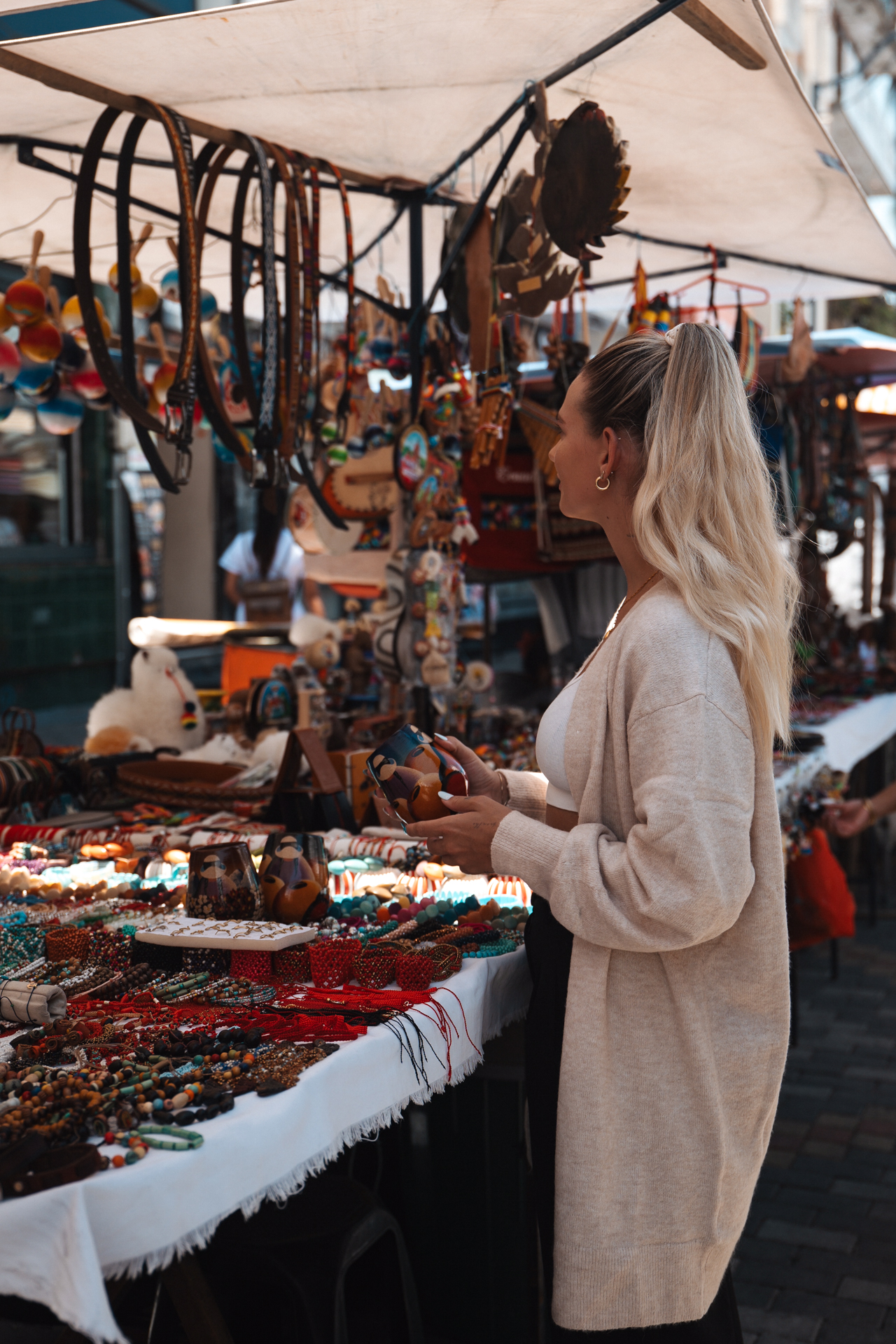 Otavalo Woman browsing a vibrant outdoor market stall in Ecuador filled with handmade crafts, jewelry, and souvenirs.