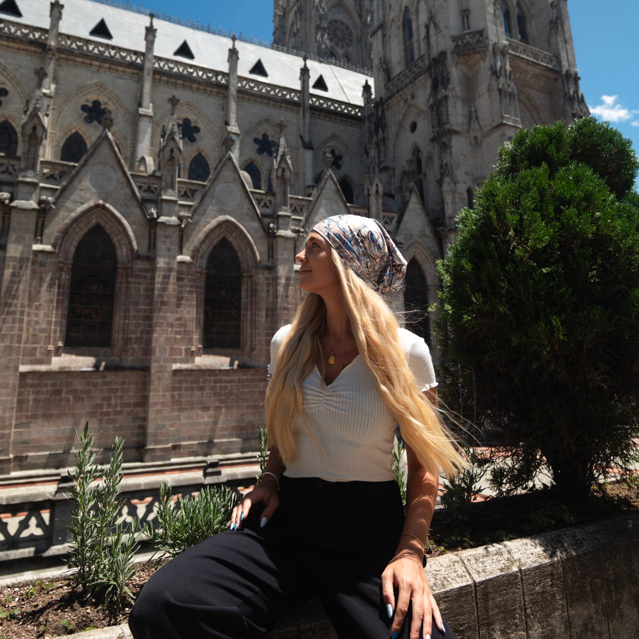 Traditions in Ecuador Woman sitting in front of the Basílica del Voto Nacional in Quito, Ecuador, with Gothic architecture and blue sky in the background.