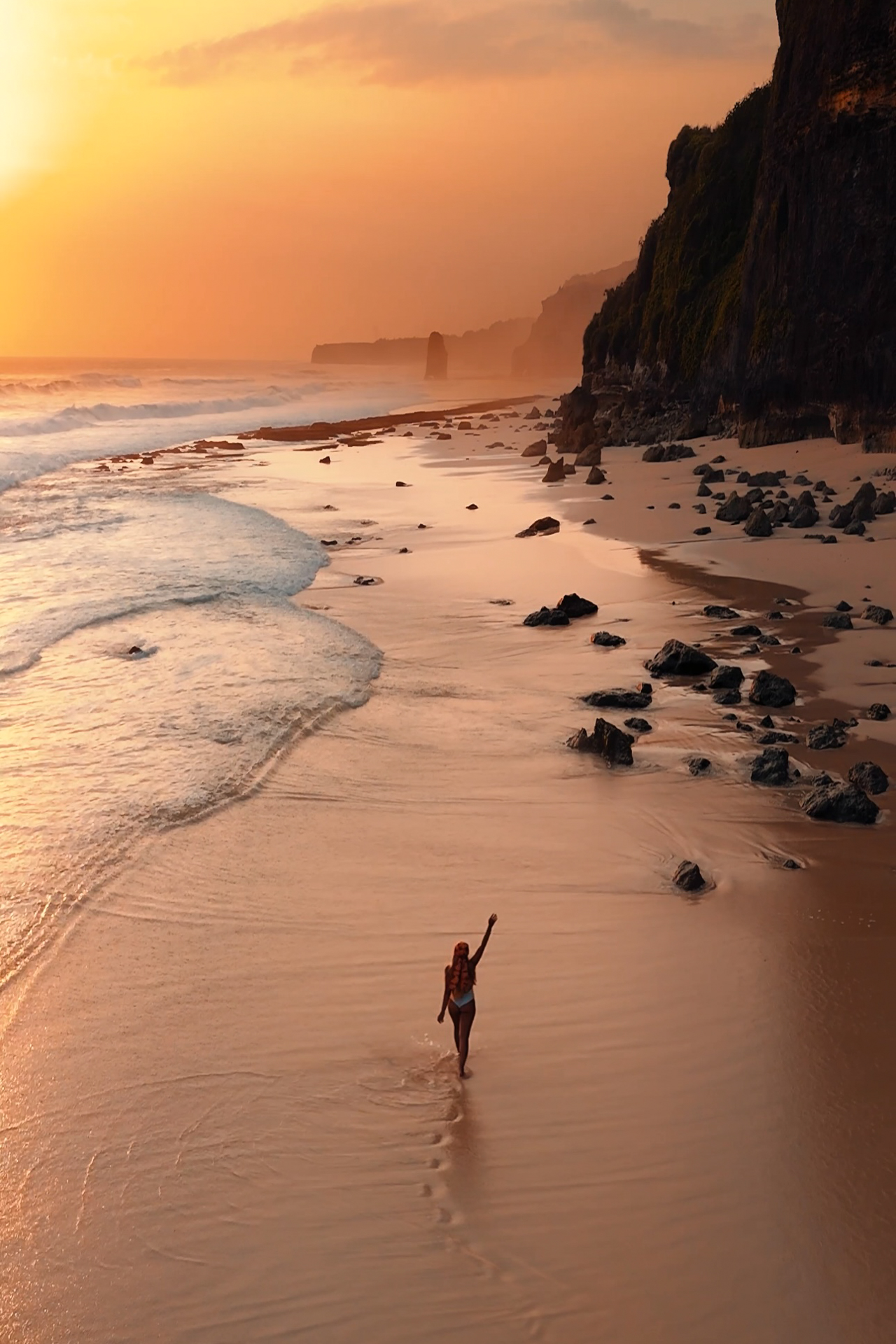 Sumba Woman walking alone along a golden sandy beach at sunset with waves crashing against the shore in Sumba.