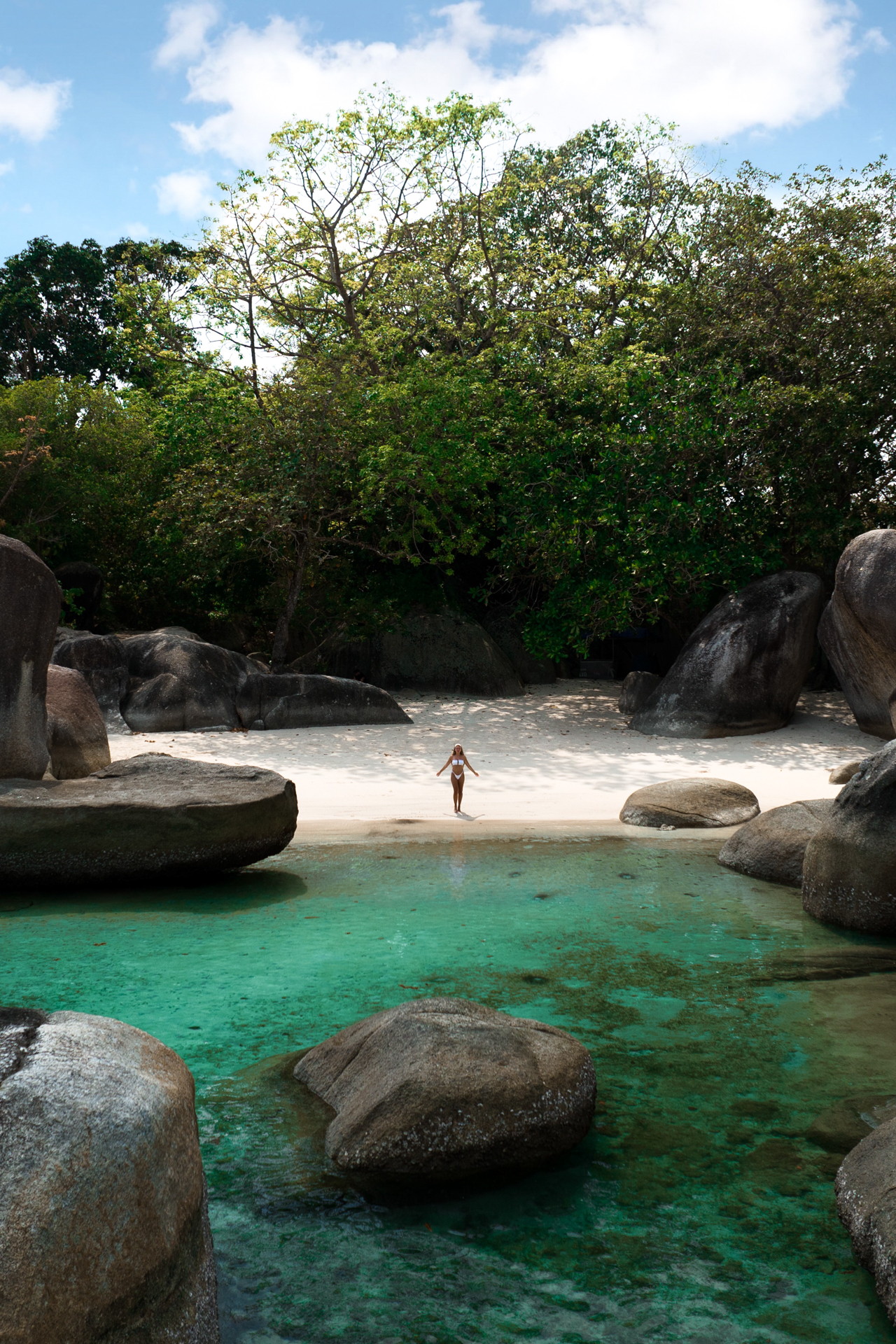 Belitung Woman standing on a white sandy beach surrounded by massive granite boulders and turquoise water in Belitung.