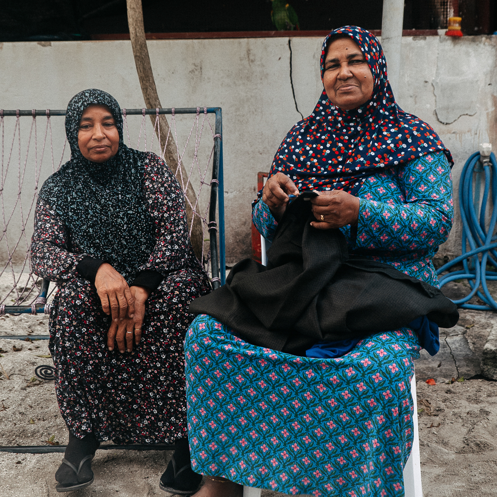 Culture in the Maldives Two Maldivian women in colorful dresses and hijabs sitting outdoors.