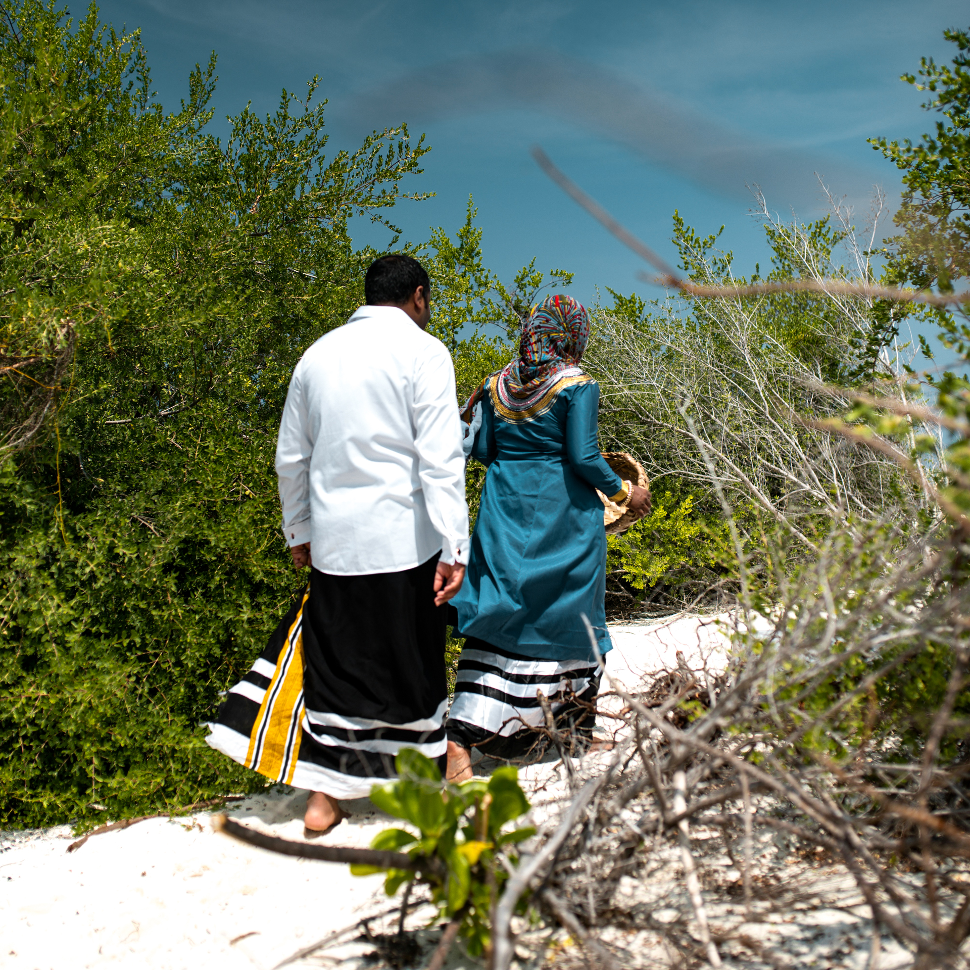 Traditions in the Maldives Maldivian couple in traditional attire walking along a sandy path.
