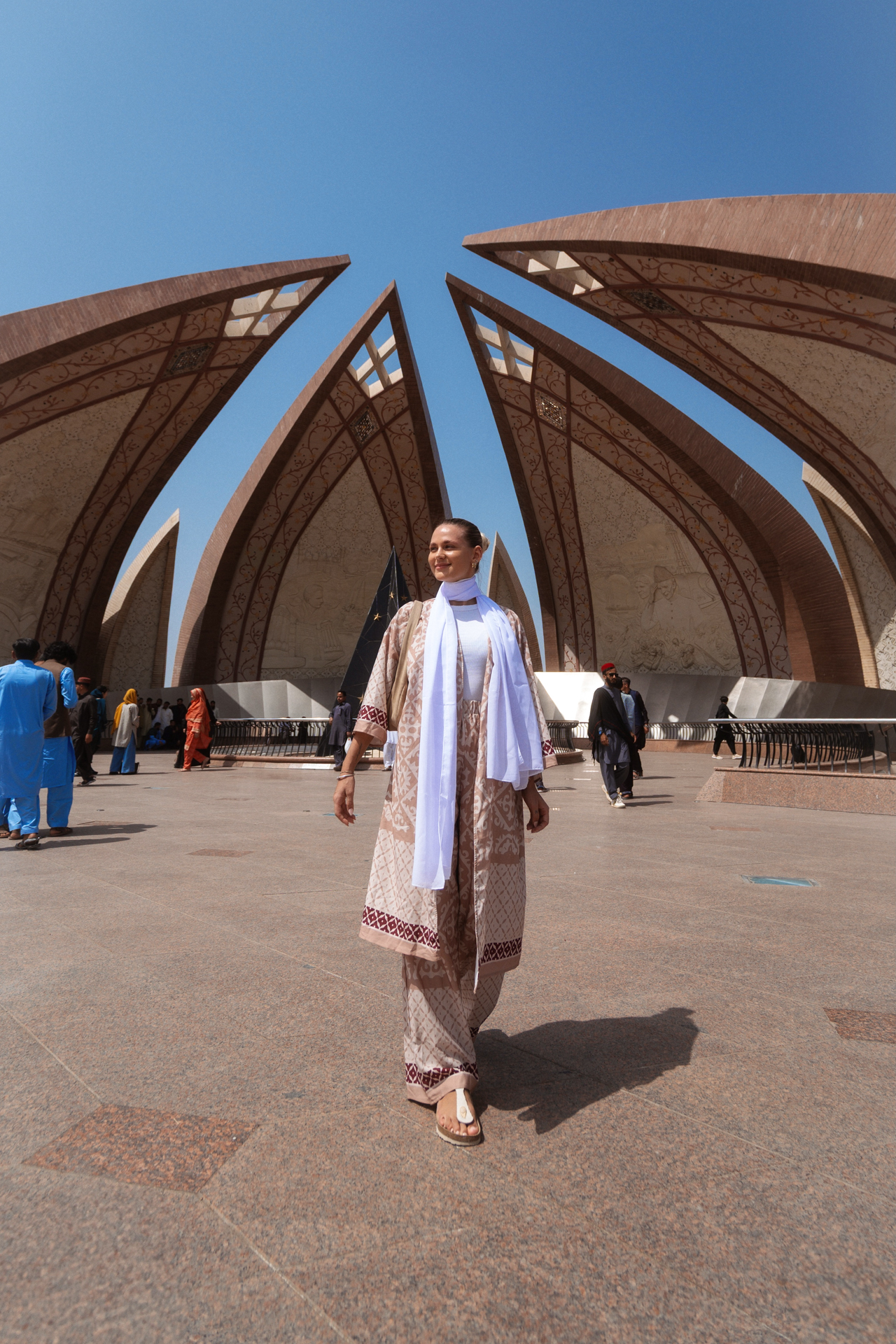 Islamabad Woman walking at the Pakistan Monument in Islamabad, Pakistan, with the national heritage structure in the background under a clear blue sky.