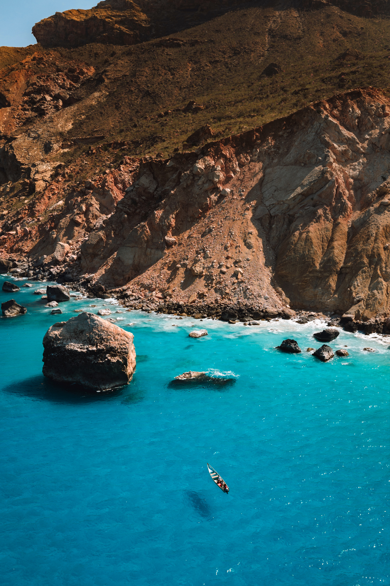Shoab coast Small boat on turquoise water with rocky cliffs and boulders along Socotra’s coast.