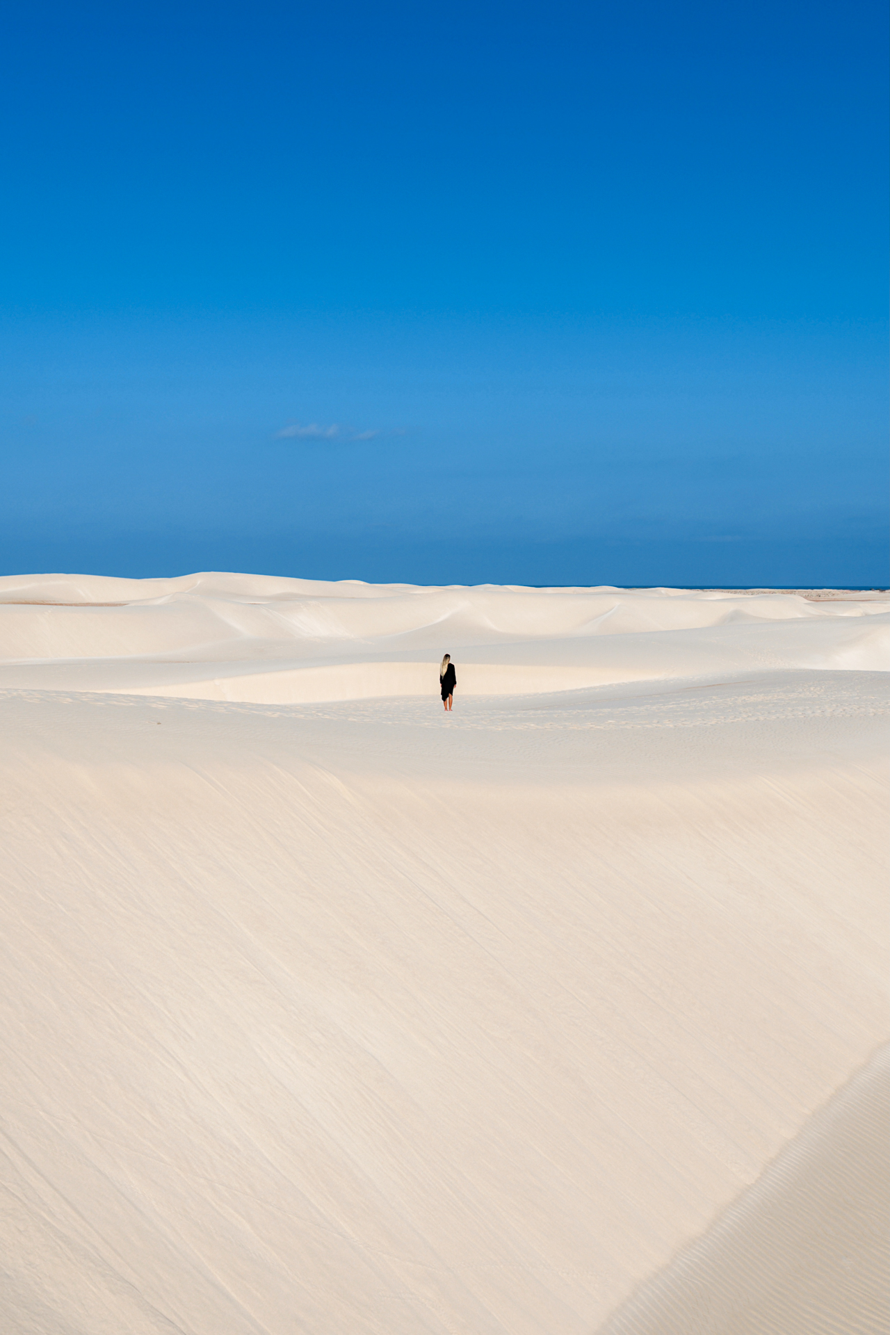 Zahek Dunes Lone traveler walking across vast white Zahek dunes under a blue sky in Socotra.