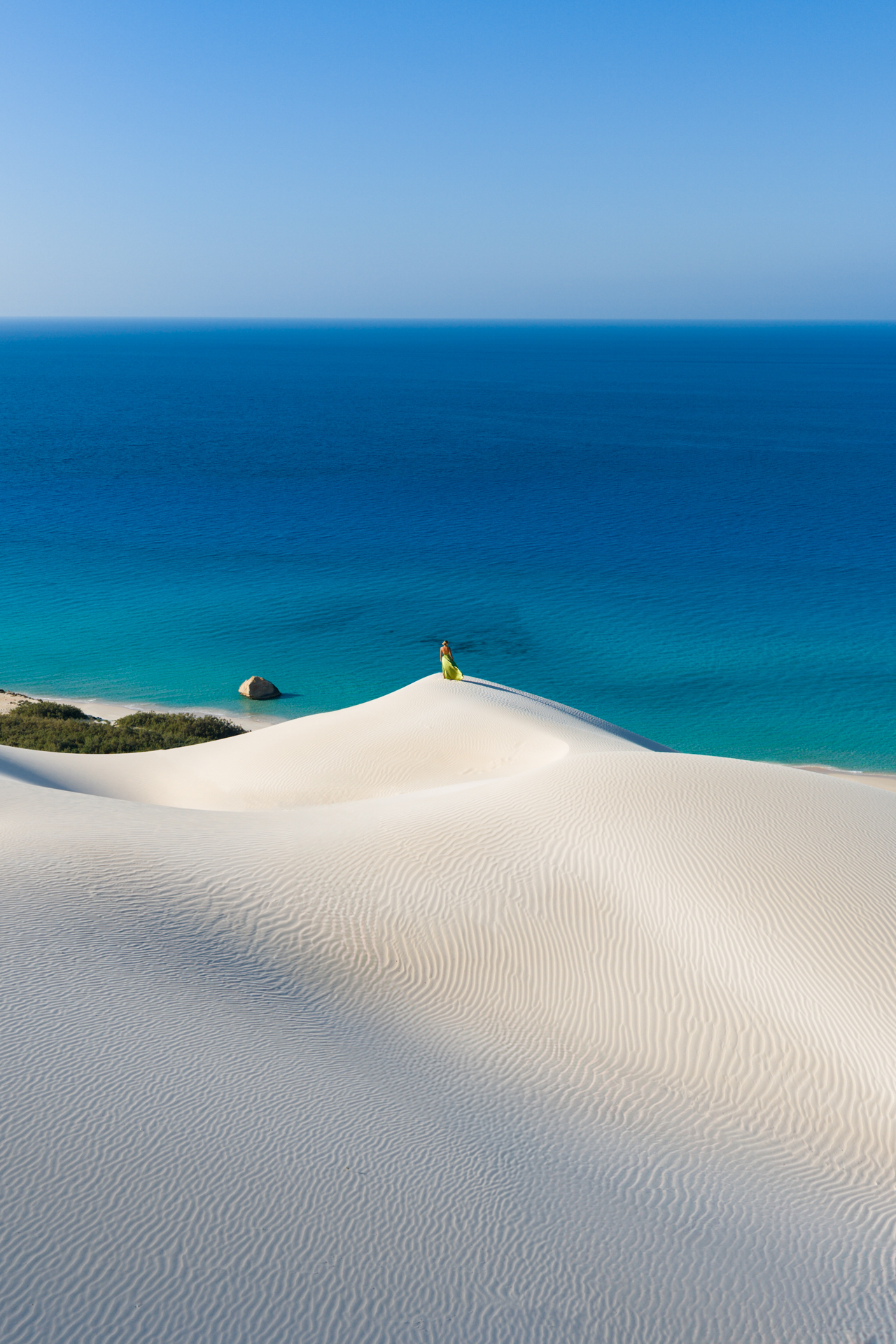 Arher Sand Dunes Woman in a green dress on top of Arher sand dunes overlooking the blue sea in Socotra.