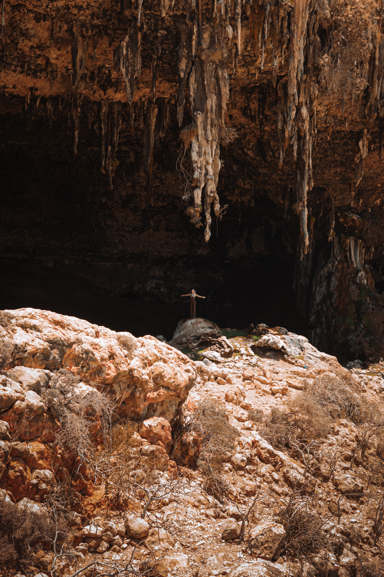 Dagub Cave Traveler standing inside Dagub cave with stalactites in Socotra’s rocky terrain.