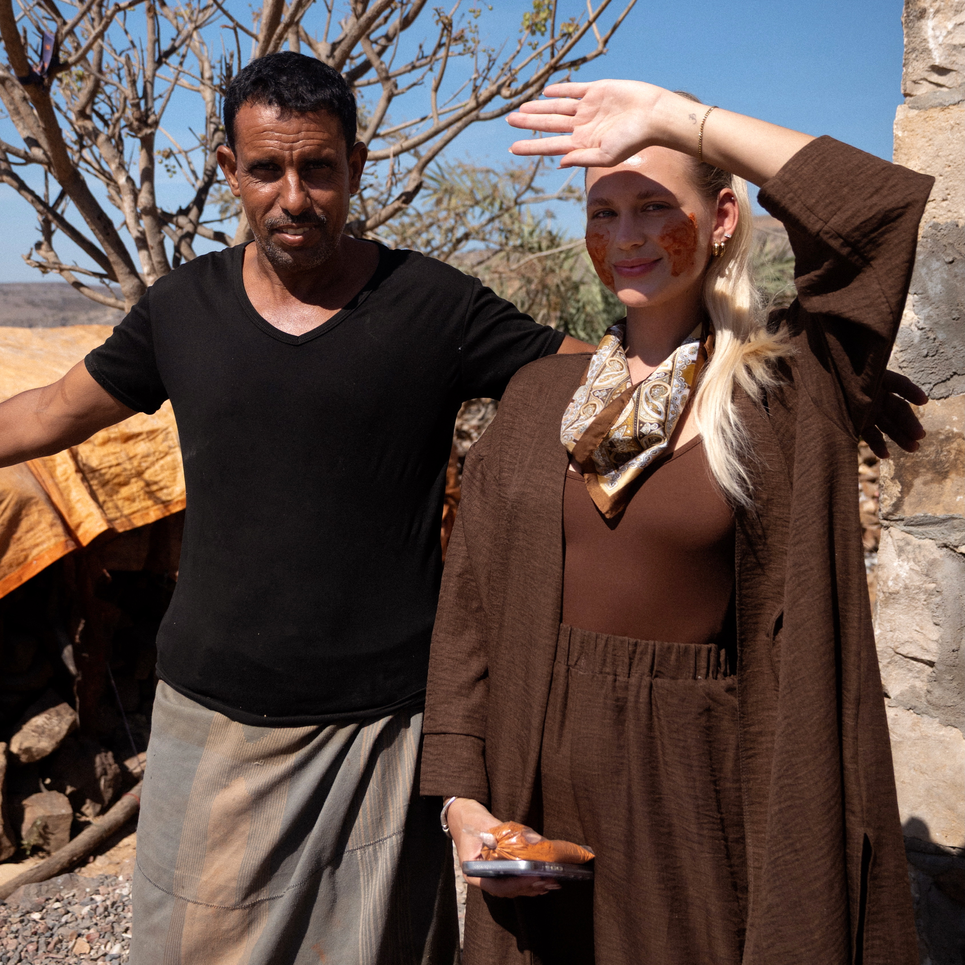 Traditions in Socotra Woman with clay mask and local man in Socotra, standing outdoors under the sun.