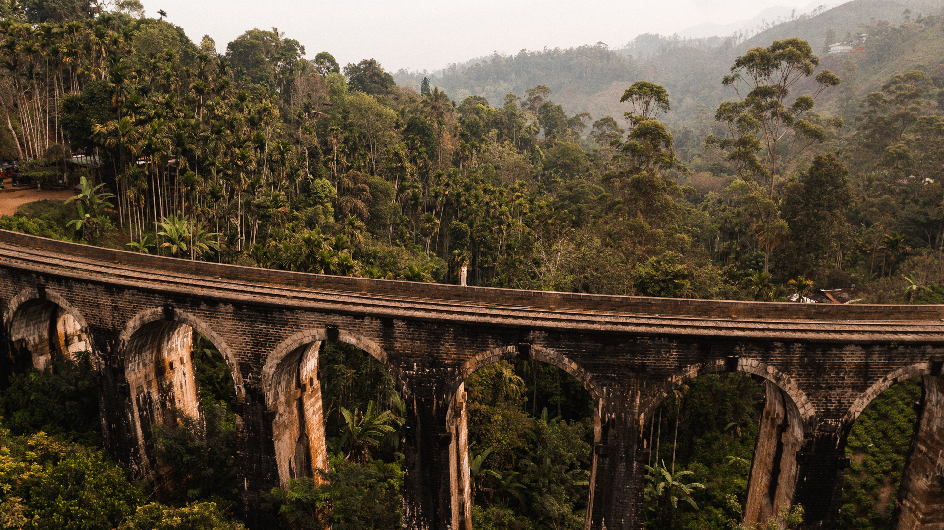 A historic stone railway bridge surrounded by lush jungle and misty hills in Ella, Sri Lanka.