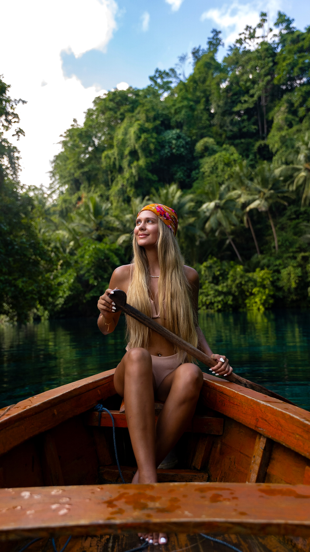 Woman paddling a wooden boat on a clear turquoise river surrounded by lush jungle in Banggai, Sulawesi, Indonesia.