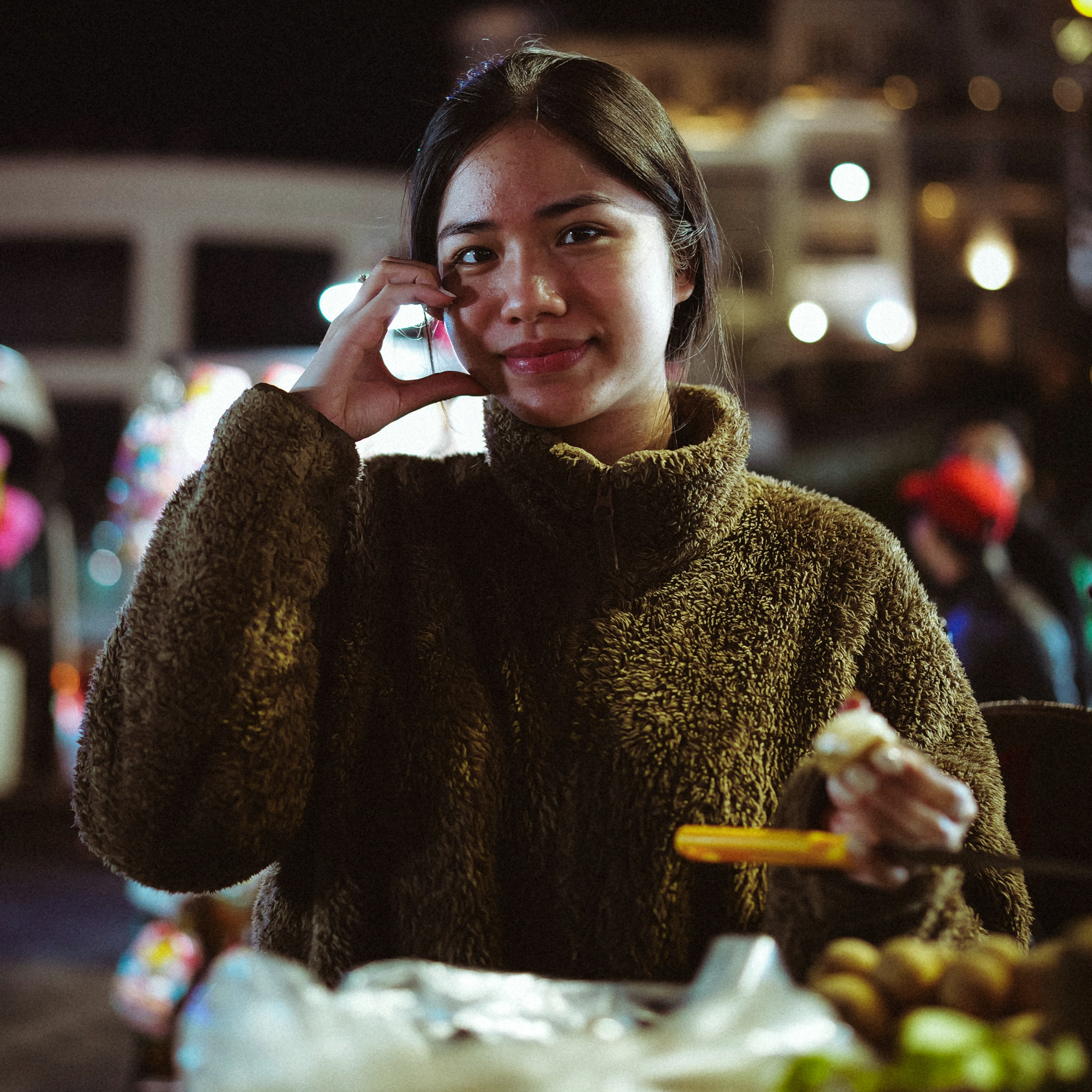 Culture in Vietnam Woman in a brown sweater smiling at a night market in Da Lat, Vietnam.