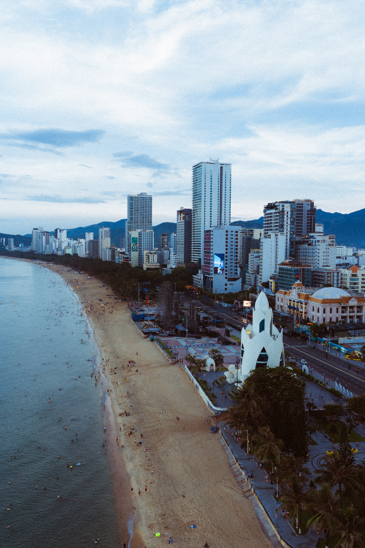 Nha Trang Aerial view of Nha Trang beach in Vietnam with skyscrapers, the iconic Tram Huong Tower, golden sand, and people swimming in the sea.