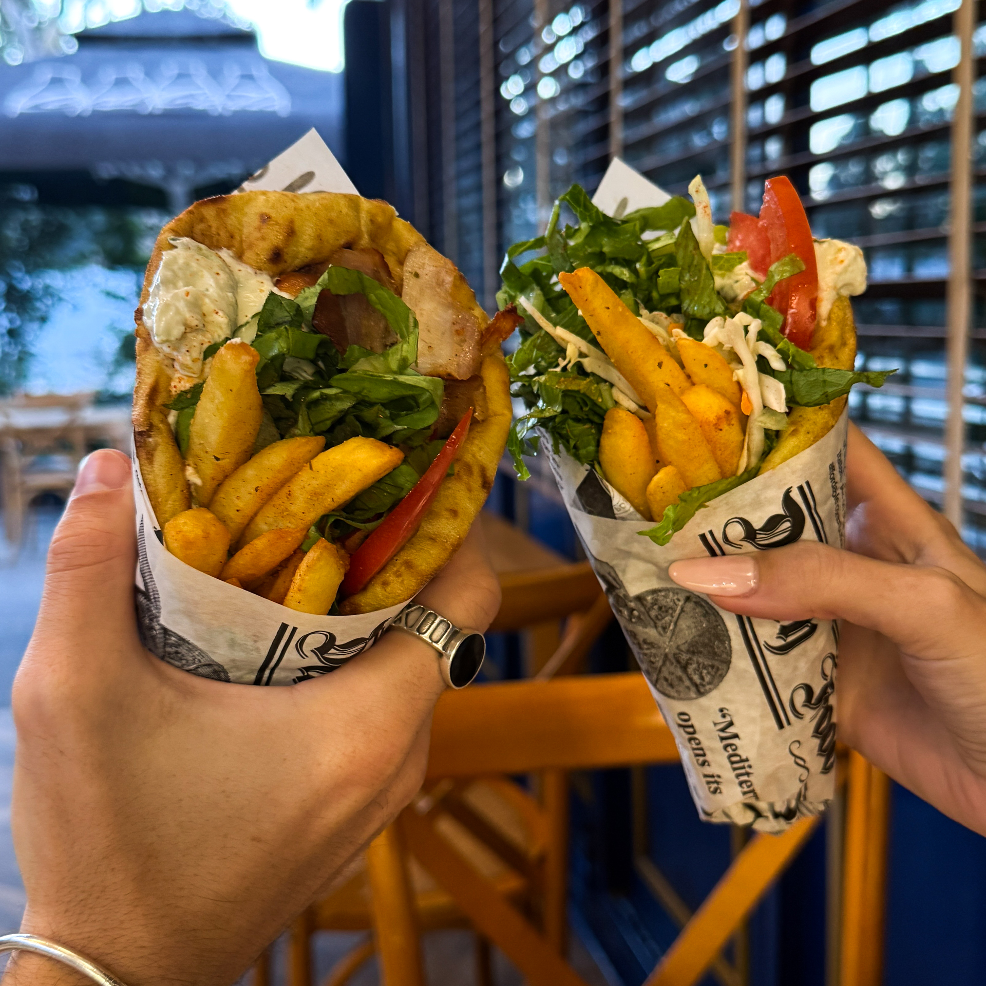 Food in Greece Two hands holding fresh Greek gyros filled with fries, vegetables, and meat wrapped in pita bread.