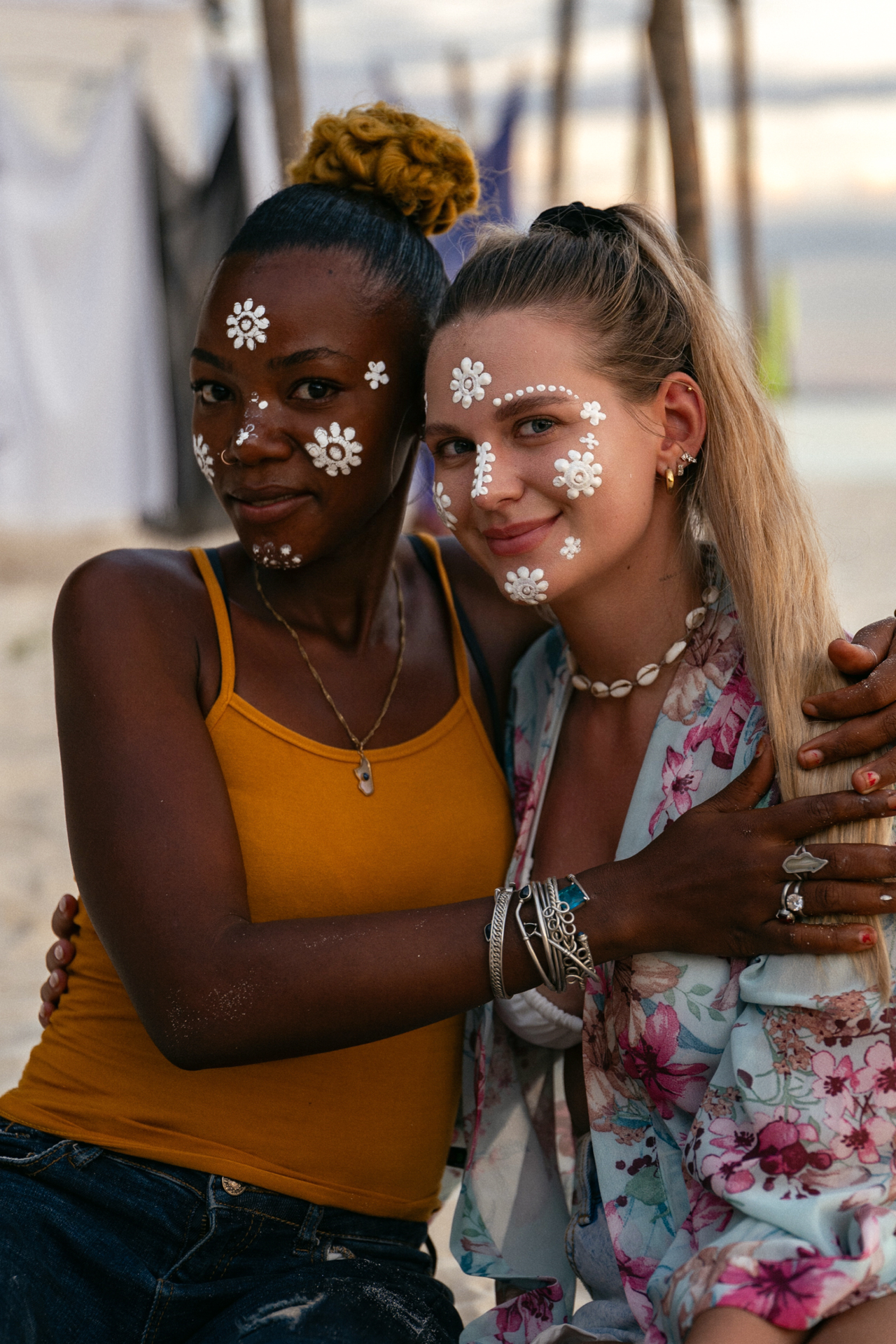 Two women with traditional white face paint smiling and embracing on a beach in Nosy Iranja, Madagascar.